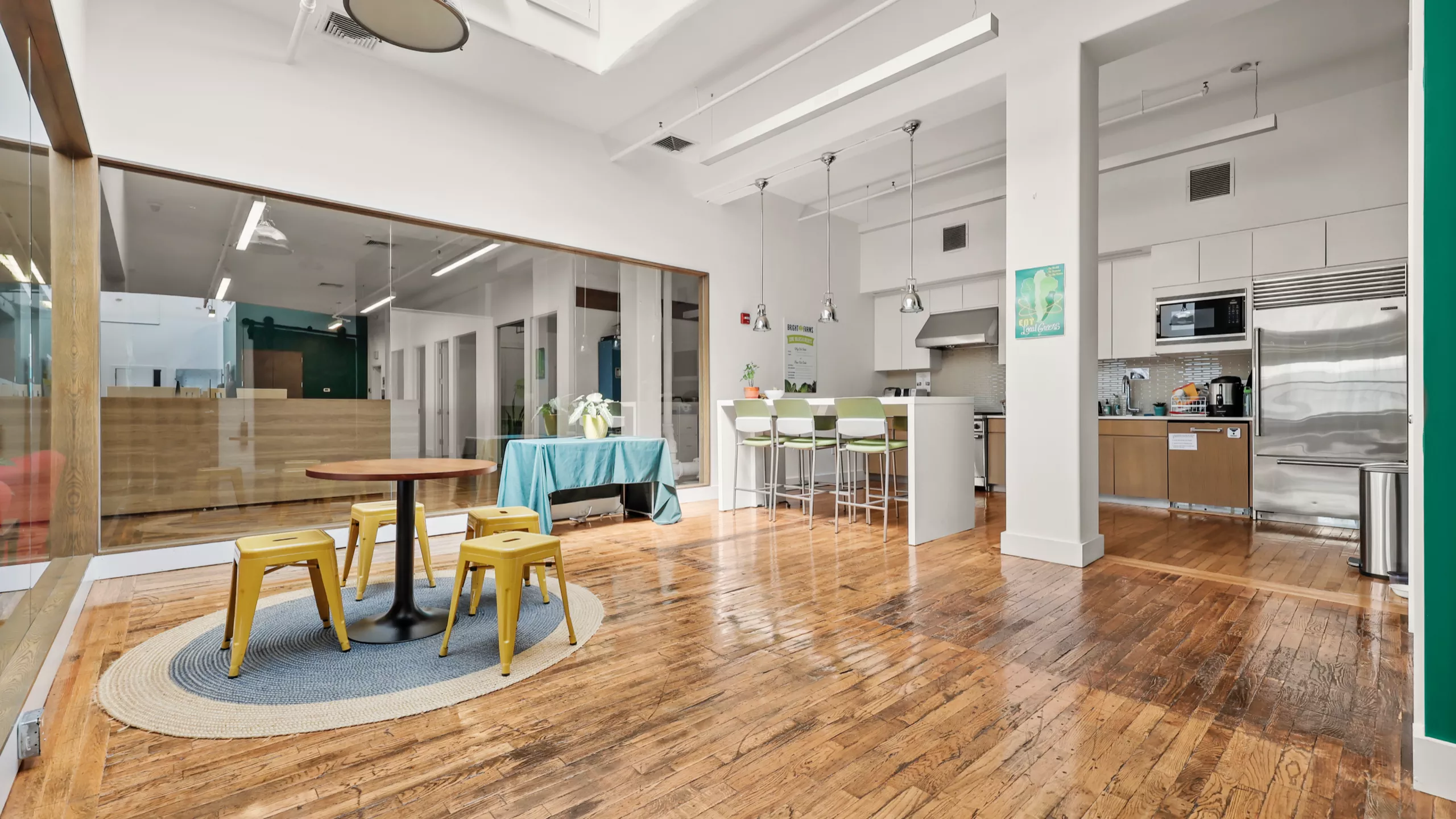 A warm and inviting communal kitchen featuring a shared dining table for colleagues to gather, eat, and connect. A counter with three green chairs offers additional seating for meals or casual conversations.