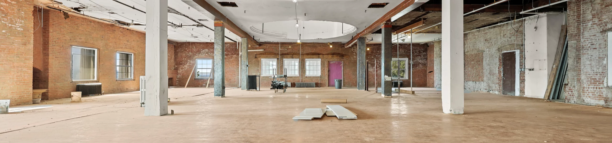 A vast, airy interior with large windows, high ceilings and abundant natural light. The raw yet promising space showcases its potential for a thoughtfully designed and functional work environment.